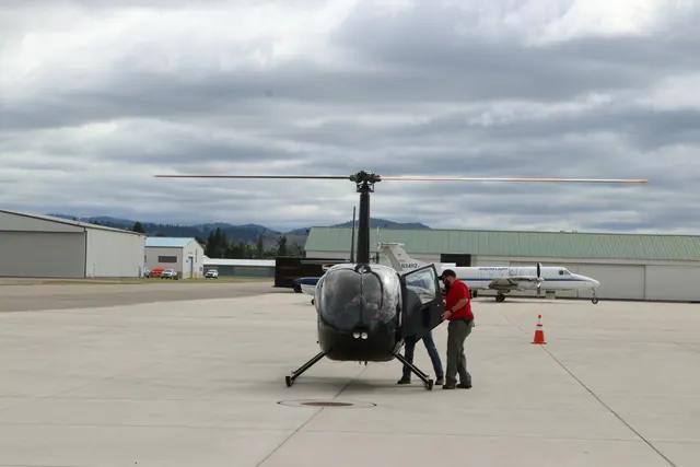 A Robinson helicopter on the ramp at an airport under a cloudy sky.